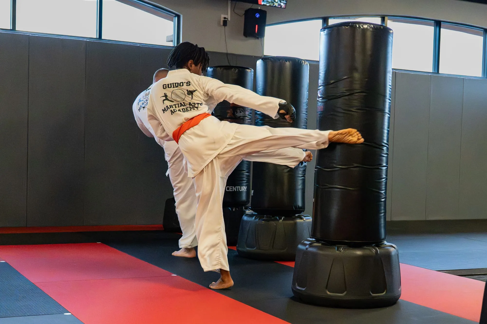 Teen and Adult MMA student throwing a high kick on a heavy bag at Guido's Martial Arts Academy in Clovis, CA