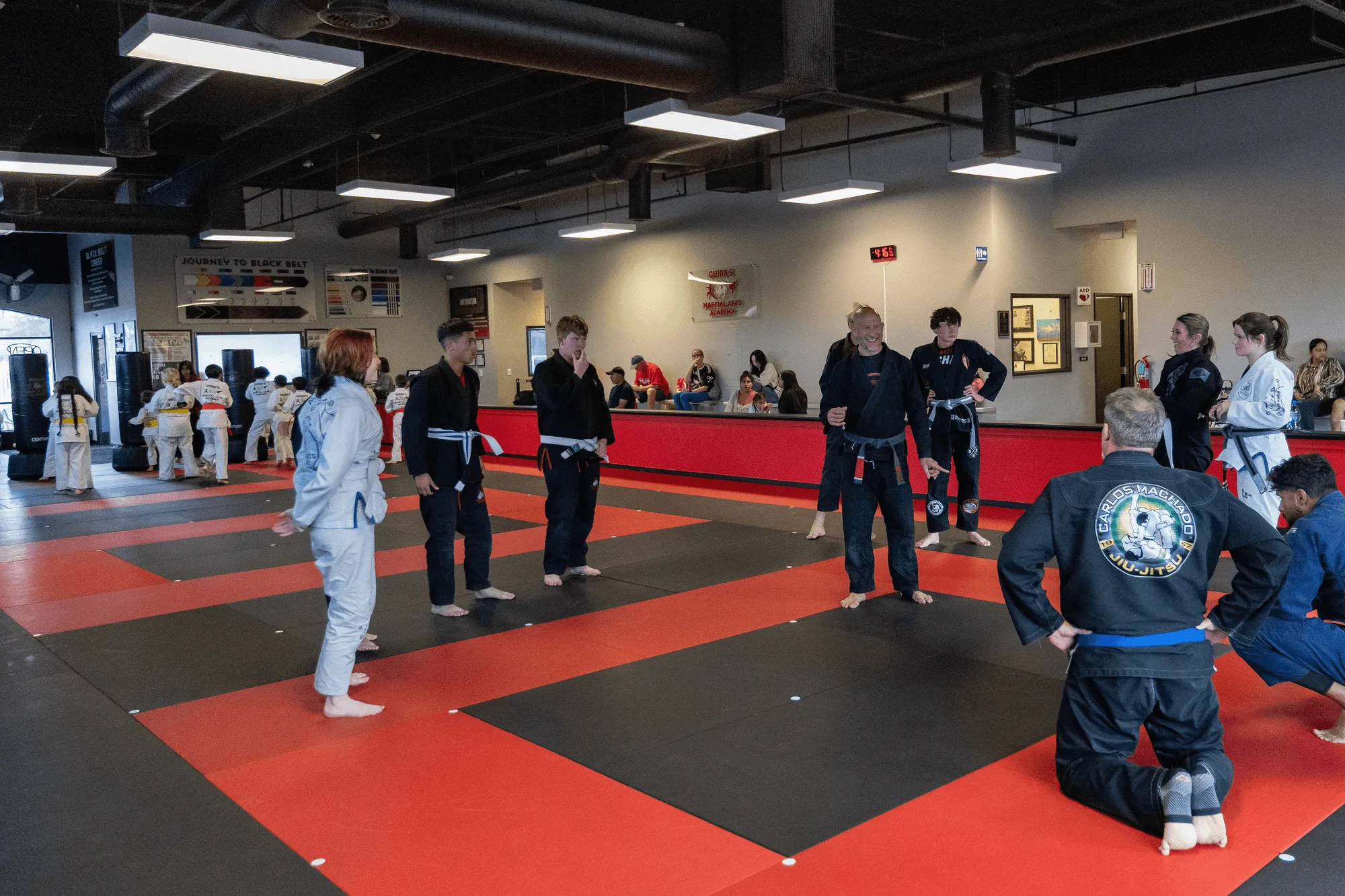 Two adult BJJ students of different builds kneeling side by side in white gis on the blue mat before class at Guido's Martial Arts Academy in Clovis, CA