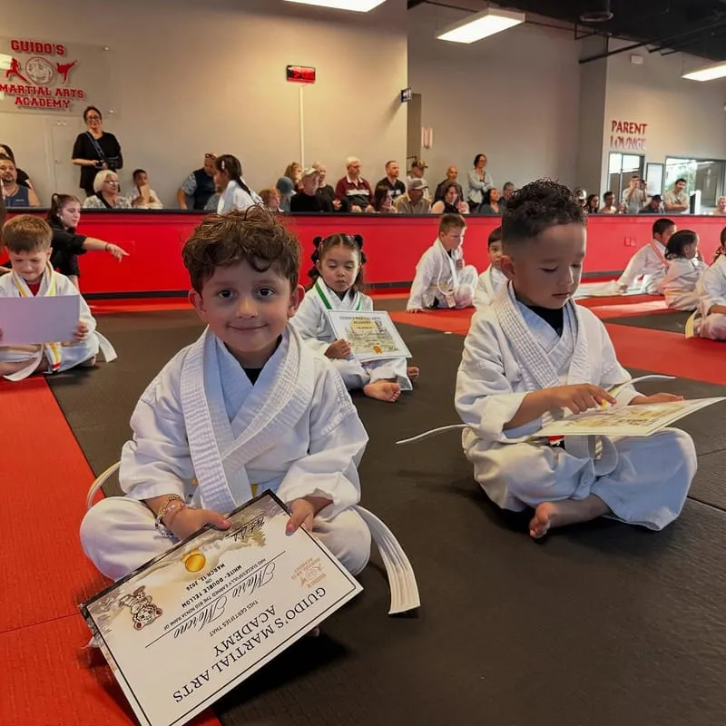 A young student smiling with a Guido's Martial Arts Academy certificate at a belt promotion in Clovis