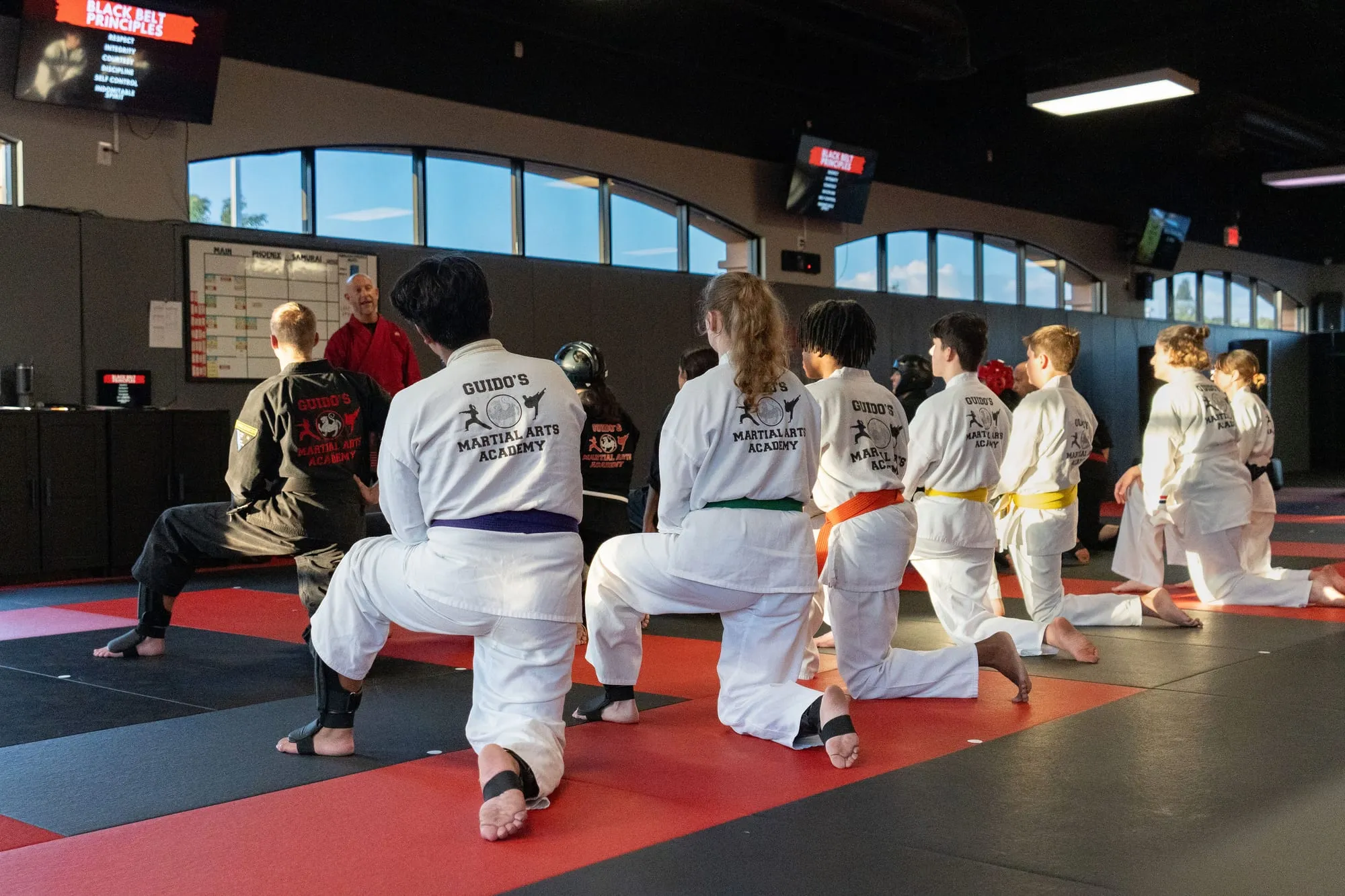 Teen and Adult MMA class lineup with fists raised in front of the Guido's Martial Arts Academy logo wall in Clovis